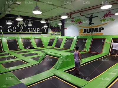 Spacious indoor freestyle trampoline park with bright green safety padding, multiple interconnected trampoline mats and jump-themed wall murals for family active play